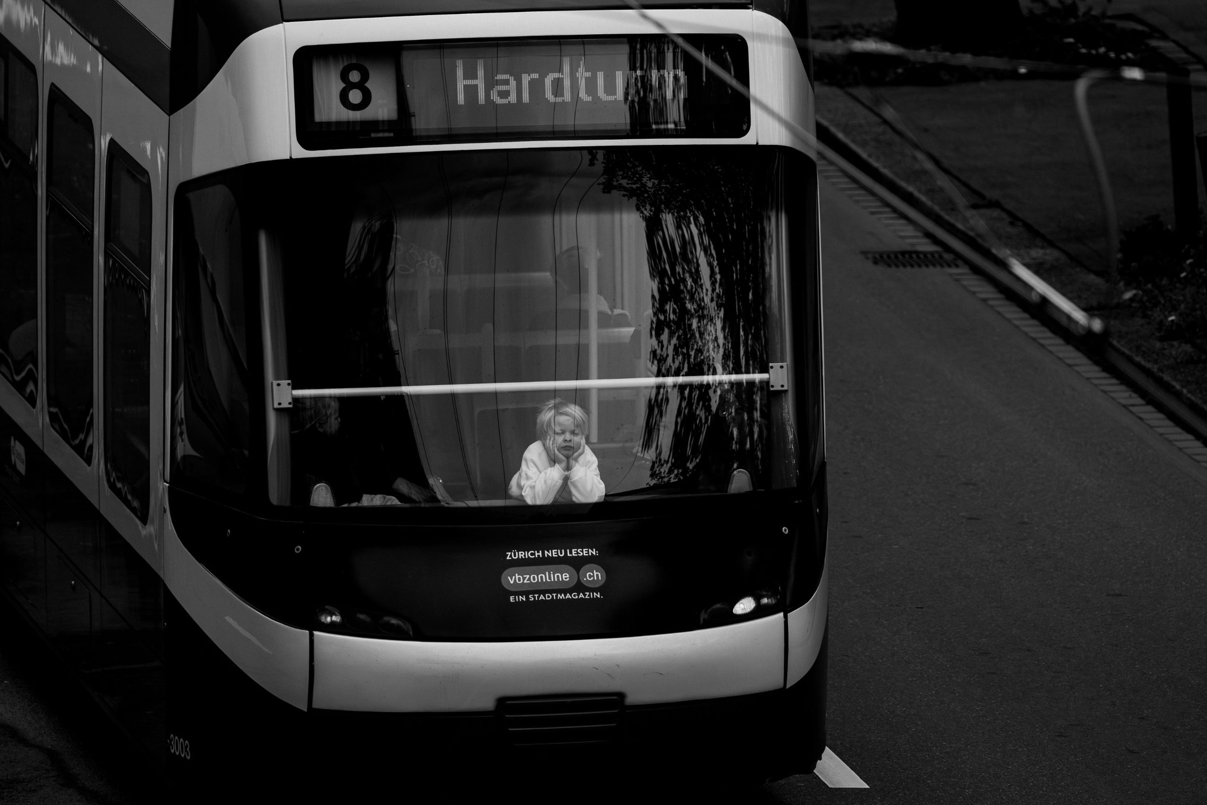 A child resting their chin in their hands at the front window of a Zurich tram, line 8 to Hardturm